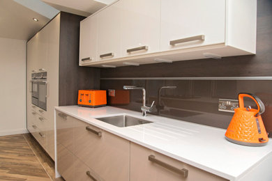 Idéer för att renovera ett stort funkis vit linjärt vitt kök med öppen planlösning, med en undermonterad diskho, släta luckor, vita skåp, bänkskiva i kvartsit, svart stänkskydd, glaspanel som stänkskydd, svarta vitvaror, ljust trägolv, en köksö och flerfärgat golv
