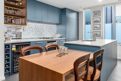 This is an example of a large modern galley kitchen/diner in Melbourne with a submerged sink, flat-panel cabinets, blue cabinets, engineered stone countertops, blue splashback, porcelain splashback, black appliances, porcelain flooring, multiple islands, grey floors and white worktops.