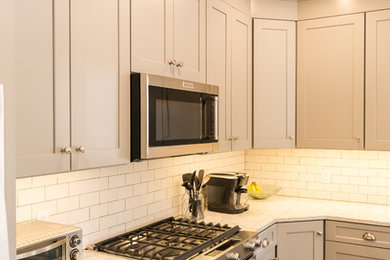 グランドラピッズにある高級な広いトランジショナルスタイルのおしゃれなキッチン (エプロンフロントシンク、シェーカースタイル扉のキャビネット、グレーのキャビネット、大理石カウンター、白いキッチンパネル、サブウェイタイルのキッチンパネル、シルバーの調理設備、茶色い床、白いキッチンカウンター) の写真