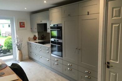 Inspiration for a mid-sized contemporary l-shaped eat-in kitchen in Hampshire with a drop-in sink, shaker cabinets, grey cabinets, quartzite benchtops, multi-coloured splashback, glass sheet splashback, stainless steel appliances, vinyl floors, a peninsula, grey floor and white benchtop.