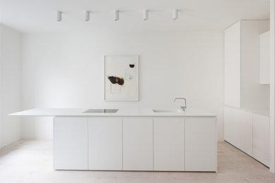 Small contemporary single-wall open plan kitchen in London with an integrated sink, composite countertops, black appliances, light hardwood flooring, an island, white floors, white worktops, flat-panel cabinets, white cabinets, white splashback, mirror splashback, a drop ceiling and feature lighting.