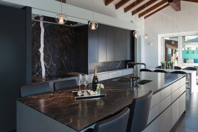 Photo of a large contemporary single-wall eat-in kitchen in Toronto with an undermount sink, flat-panel cabinets, grey cabinets, onyx benchtops, black splashback, stone slab splashback, panelled appliances, concrete floors, with island, black floor and black benchtop.