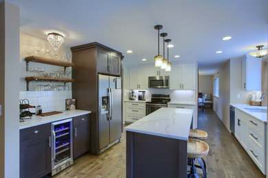 This is an example of a large contemporary u-shaped separate kitchen in Seattle with an undermount sink, shaker cabinets, white cabinets, quartz benchtops, white splashback, ceramic splashback, stainless steel appliances, medium hardwood floors, with island, brown floor and white benchtop.