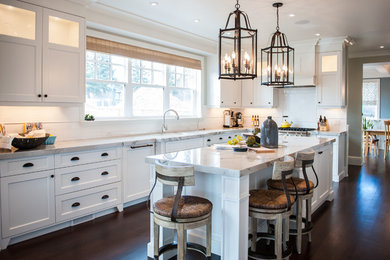 Inspiration for a large timeless l-shaped dark wood floor kitchen remodel in Calgary with an undermount sink, shaker cabinets, white cabinets, white backsplash, ceramic backsplash, stainless steel appliances and an island