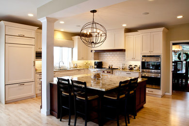 Inspiration for a large transitional l-shaped light wood floor and brown floor open concept kitchen remodel in Other with an undermount sink, shaker cabinets, white cabinets, granite countertops, white backsplash, subway tile backsplash, paneled appliances and an island