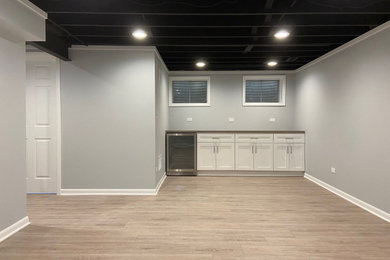 Example of a mid-sized minimalist underground laminate floor, multicolored floor and exposed beam basement design in Chicago with a bar and gray walls