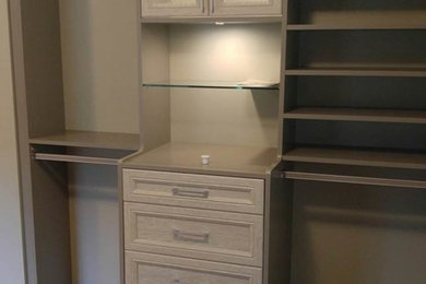 Large contemporary gender-neutral walk-in wardrobe in New York with glass-front cabinets and light hardwood floors.