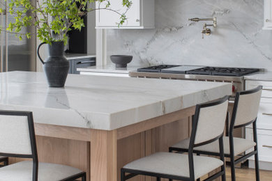 Example of a mid-sized transitional light wood floor and beige floor kitchen design in St Louis with an undermount sink, shaker cabinets, light wood cabinets, quartzite countertops, white backsplash, stone slab backsplash, stainless steel appliances, an island and multicolored countertops