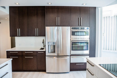 Contemporary u-shaped eat-in kitchen in Miami with an undermount sink, flat-panel cabinets, dark wood cabinets, solid surface benchtops, white splashback, stainless steel appliances, vinyl floors and a peninsula.