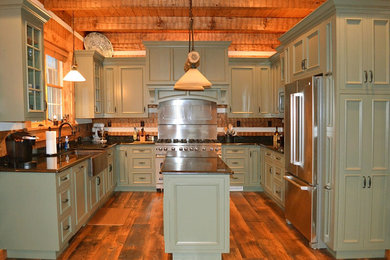Enclosed kitchen - large rustic u-shaped medium tone wood floor enclosed kitchen idea in Other with a farmhouse sink, green cabinets, granite countertops, stainless steel appliances, an island, recessed-panel cabinets, brown backsplash and wood backsplash