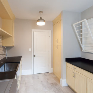 ワシントンD.C.のカントリー風おしゃれな洗濯室 (エプロンフロントシンク、インセット扉のキャビネット、黄色いキャビネット、ベージュの壁、左右配置の洗濯機・乾燥機、ベージュの床、黒いキッチンカウンター) の写真