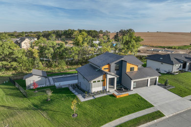 Example of a large minimalist gray house exterior design in Omaha with a black roof