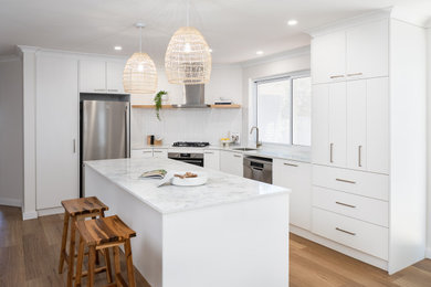 Photo of a mid-sized galley eat-in kitchen in Perth with an undermount sink, marble benchtops, white splashback, ceramic splashback, stainless steel appliances, medium hardwood floors, with island, brown floor and white benchtop.