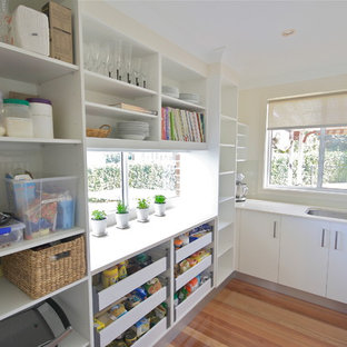 Cette photo montre une arrière-cuisine chic en U de taille moyenne avec un évier encastré, un placard sans porte, des portes de placard blanches, un plan de travail en quartz modifié, un sol en bois brun, un électroménager en acier inoxydable et aucun îlot.