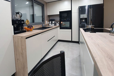 Idée de décoration pour une grande cuisine ouverte minimaliste en L avec un évier 1 bac, un placard à porte affleurante, des portes de placard blanches, un plan de travail en stratifié, une crédence en bois, un électroménager noir, un sol en carrelage de céramique, îlot et un sol beige.