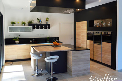 Idée de décoration pour une cuisine ouverte encastrable design en L et bois clair de taille moyenne avec un évier intégré, un placard à porte plane, un plan de travail en granite, une crédence noire, un sol en travertin, îlot et un sol beige.