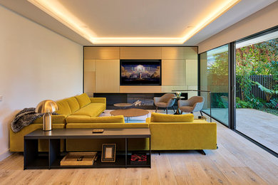 Imagen de salón para visitas cerrado actual con paredes blancas, suelo de madera clara, chimenea lineal, marco de chimenea de yeso, pared multimedia y suelo beige