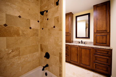 Mid-sized elegant beige tile and stone tile travertine floor and beige floor bathroom photo with raised-panel cabinets, medium tone wood cabinets, a two-piece toilet, yellow walls, an undermount sink and granite countertops