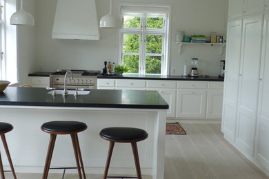 Mid-sized traditional eat-in kitchen in Copenhagen with raised-panel cabinets, white cabinets, granite benchtops, with island and black benchtop.