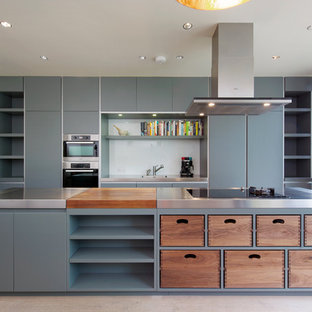 Foto de cocina actual, grande, con fregadero integrado, armarios con paneles lisos, puertas de armario grises, encimera de acero inoxidable, salpicadero blanco, salpicadero de vidrio templado, electrodomésticos de acero inoxidable y una isla