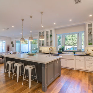 Large transitional eat-in kitchen designs - Example of a large transitional u-shaped medium tone wood floor eat-in kitchen design in Los Angeles with a farmhouse sink, glass-front cabinets, white cabinets, solid surface countertops, multicolored backsplash, porcelain backsplash, stainless steel appliances and an island