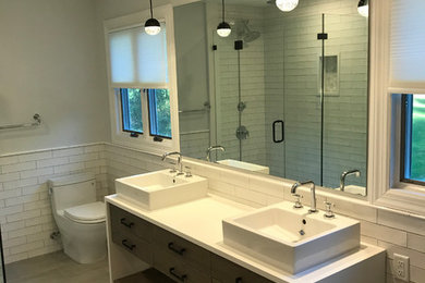 Inspiration for a mid-sized contemporary master white tile and subway tile laminate floor and brown floor corner shower remodel in New York with flat-panel cabinets, dark wood cabinets, gray walls, a vessel sink, solid surface countertops and a hinged shower door