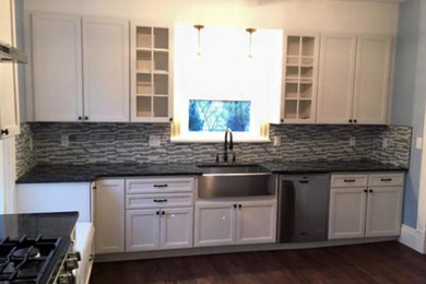 Inspiration for a mid-sized transitional l-shaped medium tone wood floor and brown floor kitchen pantry remodel in Other with a farmhouse sink, recessed-panel cabinets, white cabinets, granite countertops, multicolored backsplash, glass tile backsplash, stainless steel appliances, no island and black countertops