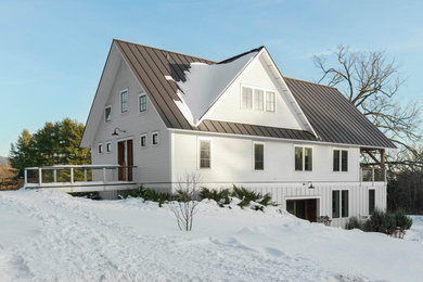 Photo of a country three-storey white house exterior in Burlington with a metal roof and a gable roof.
