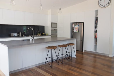Photo of a mid-sized modern l-shaped eat-in kitchen in Sydney with an undermount sink, flat-panel cabinets, white cabinets, granite benchtops, black splashback, mirror splashback, stainless steel appliances, medium hardwood floors and with island.