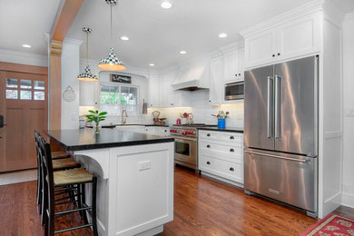Example of a mid-sized cottage u-shaped medium tone wood floor and brown floor open concept kitchen design in San Francisco with shaker cabinets, white cabinets, stainless steel appliances, a peninsula, a farmhouse sink, white backsplash, subway tile backsplash and black countertops