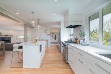 Large trendy l-shaped medium tone wood floor open concept kitchen photo in Portland with an undermount sink, flat-panel cabinets, white cabinets, quartzite countertops, white backsplash, stone slab backsplash, stainless steel appliances and an island