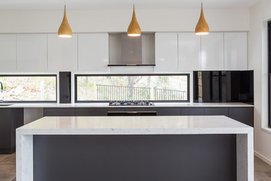 This is an example of a large contemporary single-wall open plan kitchen in Gold Coast - Tweed with a single-bowl sink, recessed-panel cabinets, white cabinets, glass sheet splashback, stainless steel appliances, ceramic floors and with island.