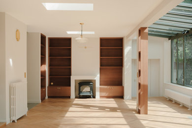 Inspiration pour un salon blanc et bois design en bois de taille moyenne et ouvert avec une bibliothèque ou un coin lecture, un mur beige, parquet clair, un poêle à bois, un manteau de cheminée en plâtre et un téléviseur encastré.