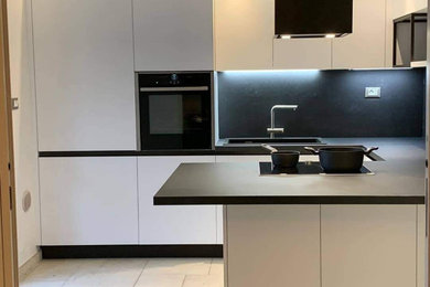 Idee per una cucina ad U moderna chiusa e di medie dimensioni con lavello a vasca singola, ante lisce, ante bianche, top in laminato, paraspruzzi nero, elettrodomestici neri, pavimento in gres porcellanato, pavimento grigio, top nero e soffitto ribassato