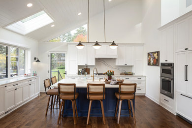 Beach style u-shaped vaulted ceiling kitchen photo in Minneapolis with a farmhouse sink, raised-panel cabinets, white backsplash and stainless steel appliances