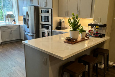 Example of a mid-sized trendy u-shaped vinyl floor and brown floor eat-in kitchen design in Orange County with an undermount sink, shaker cabinets, gray cabinets, quartzite countertops, white backsplash, quartz backsplash, colored appliances, a peninsula and white countertops