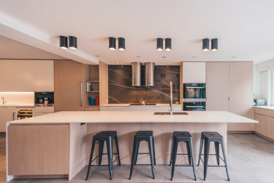 Inspiration for a large contemporary ceramic tile and gray floor eat-in kitchen remodel in Vancouver with a drop-in sink, flat-panel cabinets, light wood cabinets, black backsplash, stone slab backsplash, stainless steel appliances, an island and white countertops