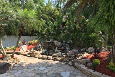 Diseño de jardín tropical de tamaño medio en patio trasero con fuente, exposición parcial al sol y adoquines de piedra natural