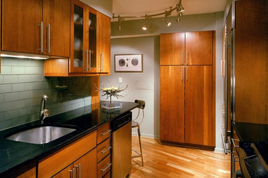 Inspiration for a contemporary galley enclosed kitchen remodel in DC Metro with an undermount sink, flat-panel cabinets, medium tone wood cabinets, granite countertops, green backsplash, glass tile backsplash and paneled appliances