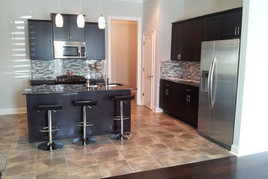 Inspiration for a mid-sized transitional single-wall ceramic tile and beige floor eat-in kitchen remodel in New Orleans with a double-bowl sink, recessed-panel cabinets, dark wood cabinets, multicolored backsplash, mosaic tile backsplash, white appliances, an island and black countertops