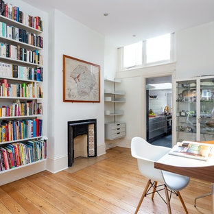 This is an example of a retro home office and library in London with white walls, medium hardwood flooring, a two-sided fireplace, a freestanding desk and brown floors.