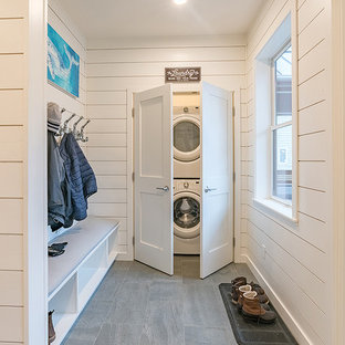 This is an example of a medium sized coastal laundry cupboard in Seattle with white walls, porcelain flooring, grey floors and a stacked washer and dryer.
