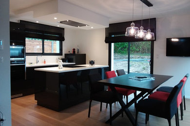 This is an example of a mid-sized transitional galley open plan kitchen in Le Havre with an integrated sink, white splashback, black appliances, light hardwood floors, with island and white benchtop.