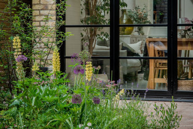Photo of a small contemporary courtyard full sun garden for summer in London with a flowerbed, brick paving and a wood fence.