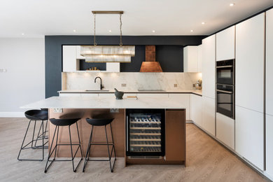 Medium sized modern l-shaped kitchen/diner in Other with flat-panel cabinets, an island, white cabinets, engineered stone countertops, white splashback, black appliances and white worktops.