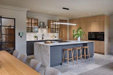 Photo of a large contemporary grey and white galley open plan kitchen in Sussex with a double-bowl sink, flat-panel cabinets, light wood cabinets, marble worktops, white splashback, porcelain splashback, integrated appliances, limestone flooring, an island, beige floors, white worktops and a feature wall.