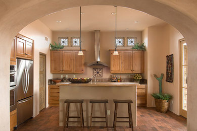 Eat-in kitchen - mid-sized rustic u-shaped brick floor and red floor eat-in kitchen idea in Albuquerque with a drop-in sink, raised-panel cabinets, light wood cabinets, wood countertops, beige backsplash, mosaic tile backsplash, stainless steel appliances and an island