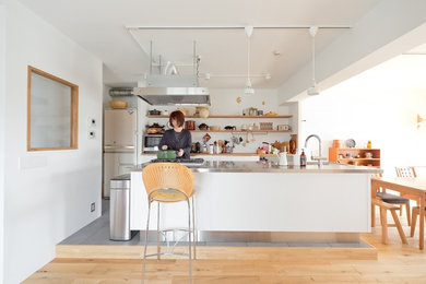 Design ideas for a scandinavian galley eat-in kitchen in Osaka with open cabinets, white cabinets, stainless steel benchtops, white splashback, stainless steel appliances, medium hardwood floors, with island, brown floor and grey benchtop.