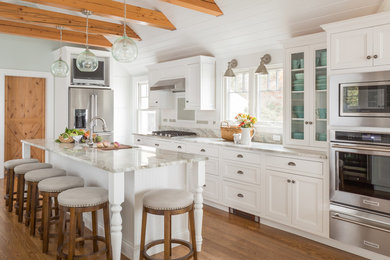 This is an example of a large beach style u-shaped open plan kitchen in Boston with an undermount sink, recessed-panel cabinets, white cabinets, white splashback, stainless steel appliances, medium hardwood floors, with island, brown floor, granite benchtops, ceramic splashback and beige benchtop.