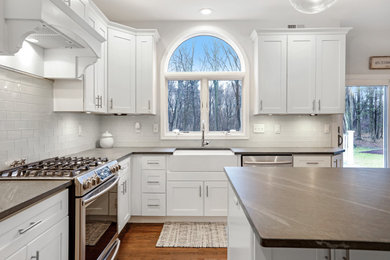 Eat-in kitchen - large transitional l-shaped medium tone wood floor and brown floor eat-in kitchen idea in New York with a farmhouse sink, shaker cabinets, white cabinets, soapstone countertops, white backsplash, subway tile backsplash, stainless steel appliances, an island and multicolored countertops